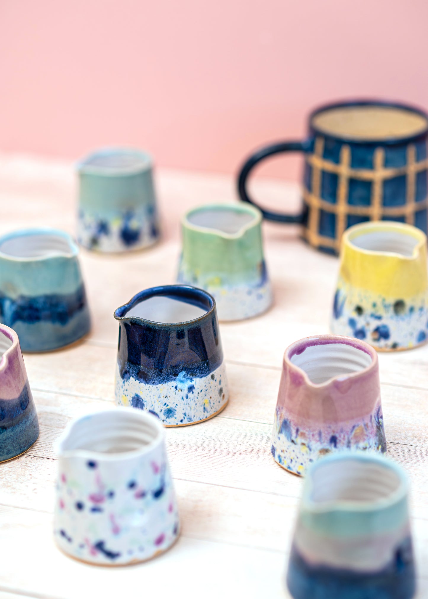 Collection of colorful ceramic containers on a light surface with a pink background