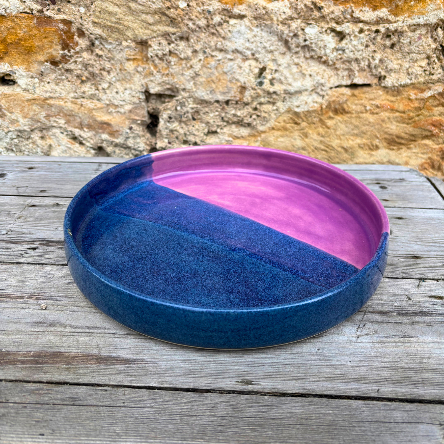 Ceramic tray with blue and pink gradient on a wooden surface with stone wall background