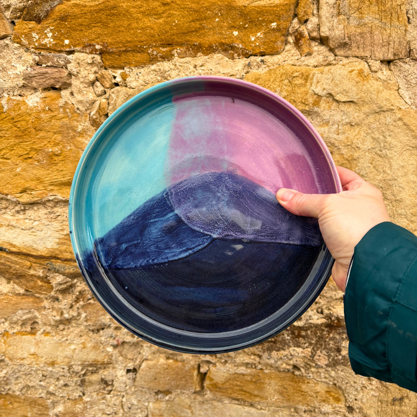 Hand holding a colorful ceramic tray against a stone wall background