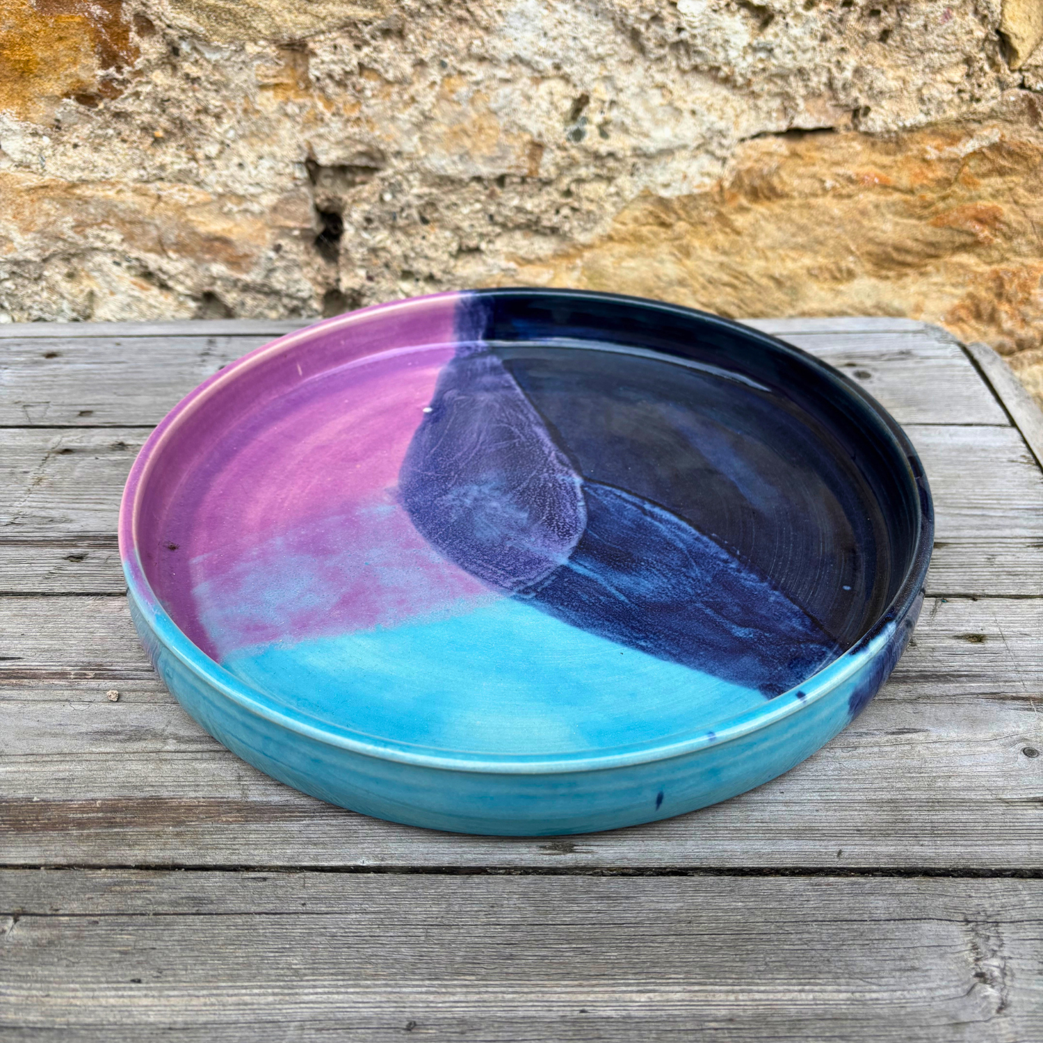 Colorful ceramic tray with purple, blue, and black gradient on a wooden surface with stone background