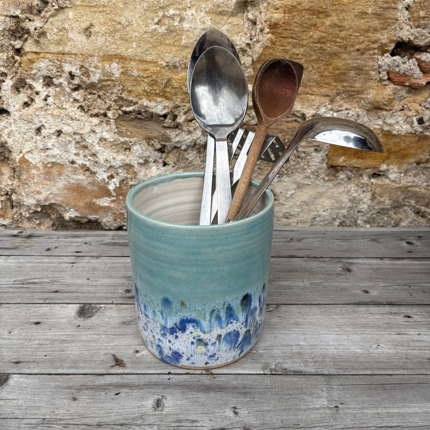Ceramic container with spoons against a stone wall