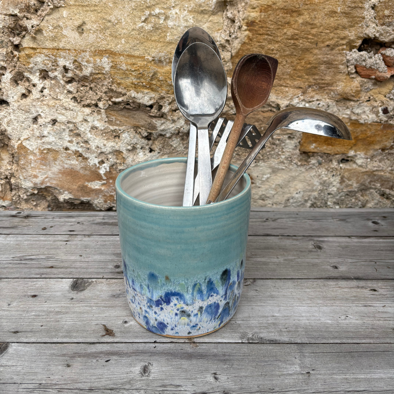 Ceramic container with spoons against a stone wall