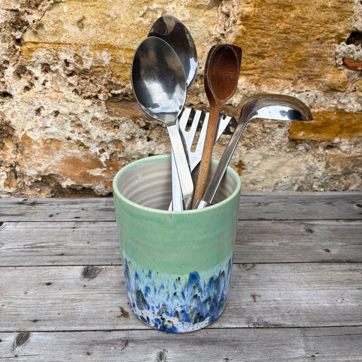 Green ceramic container with silver and wooden utensils against a stone wall background