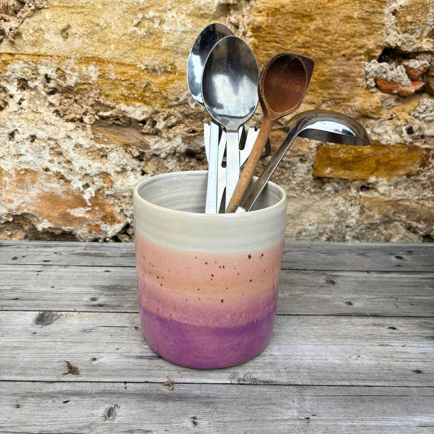 Ceramic utensil holder with gradient color and cutlery against a stone wall background