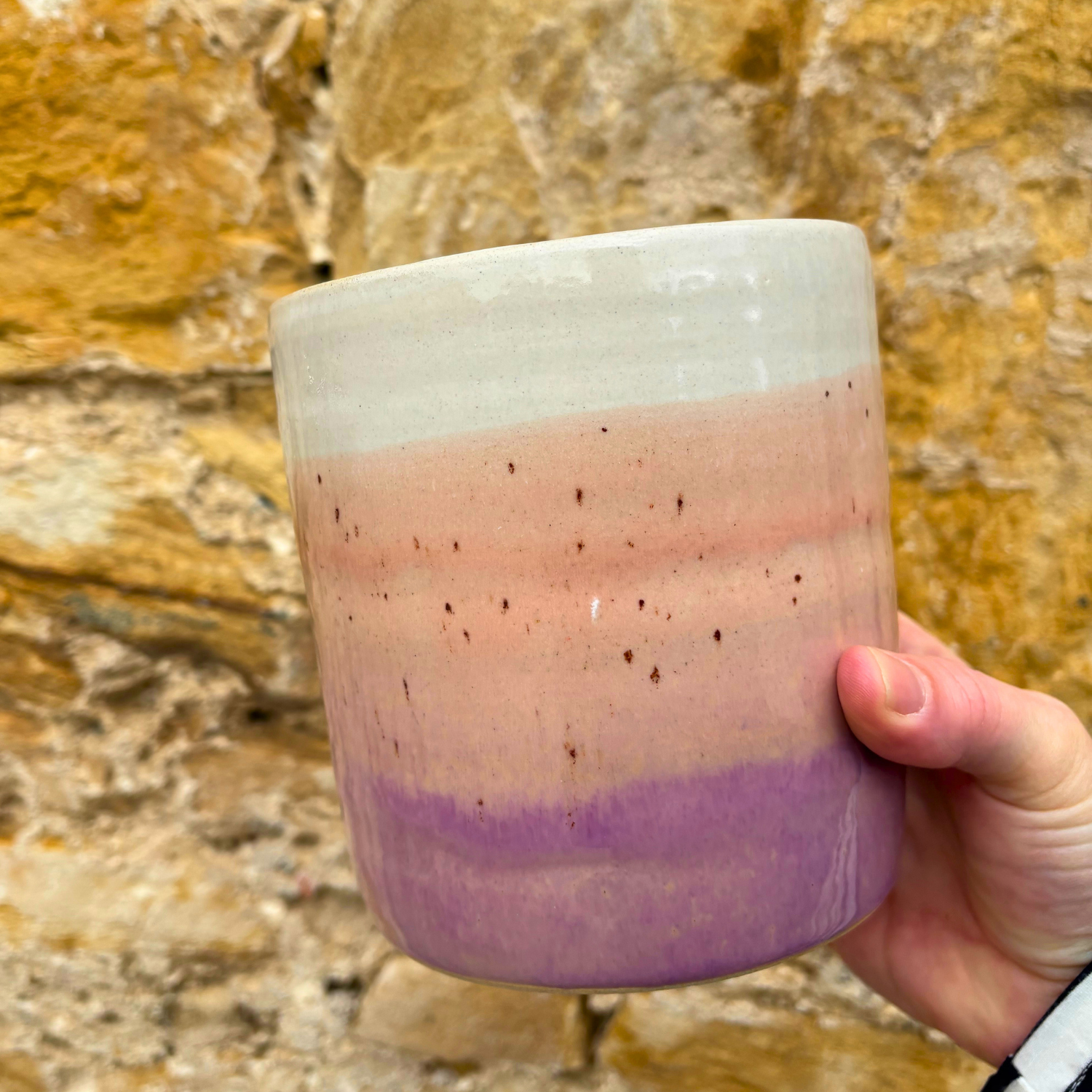 Hand holding a ceramic utensil pot  with a gradient design against a stone wall background
