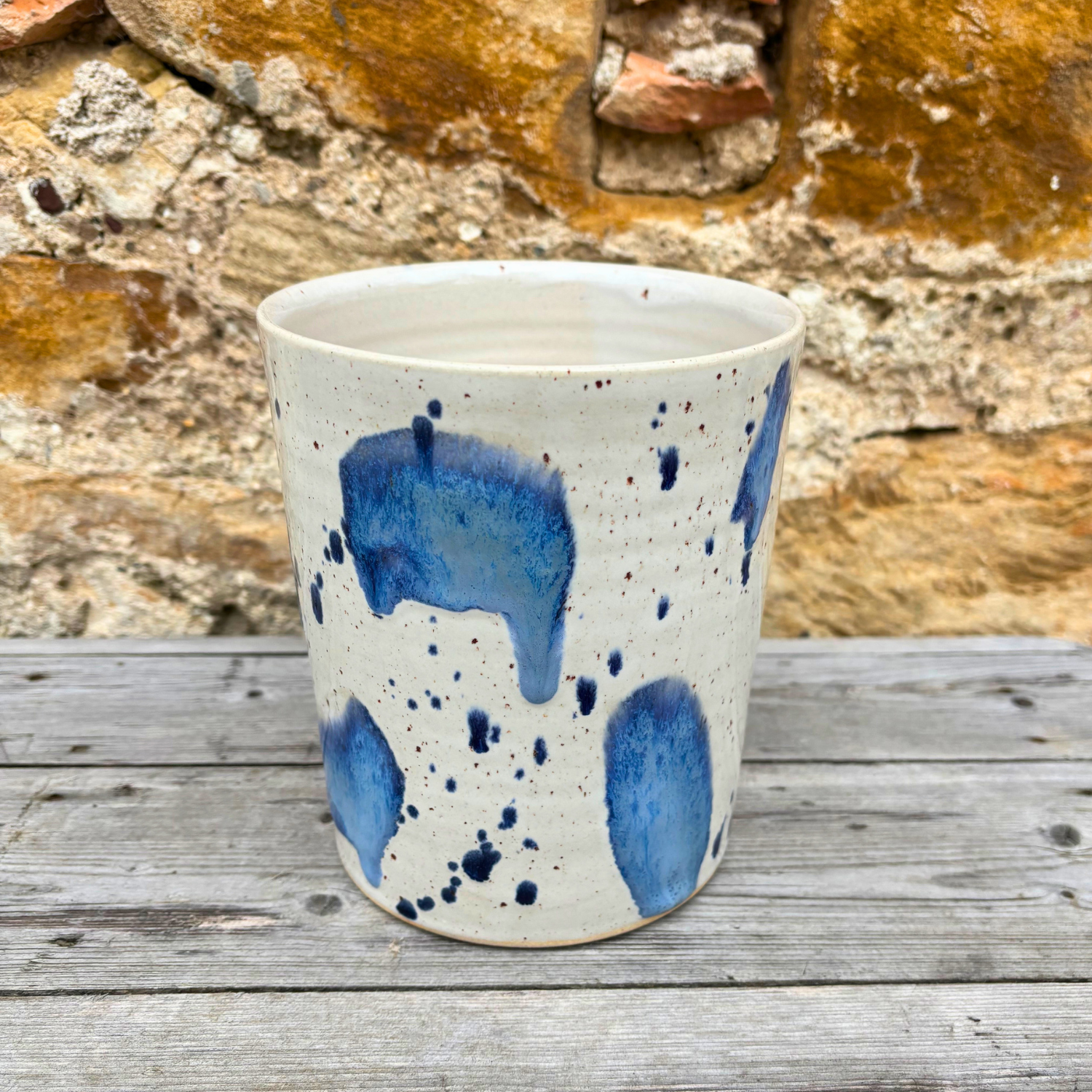 Ceramic utensil pot with blue splashes on a wooden surface with a stone wall background