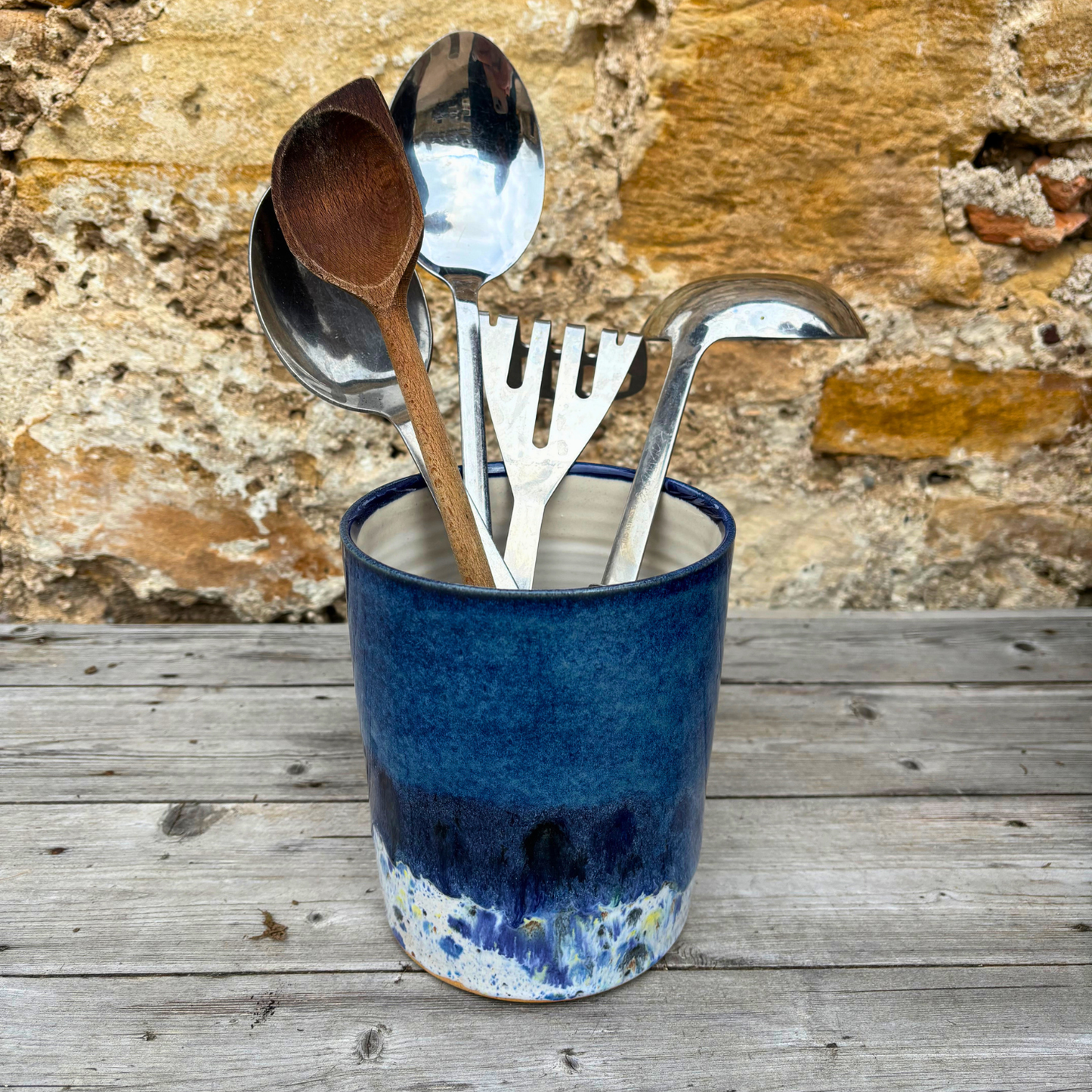 Blue ceramic container with kitchen utensils against a stone wall background