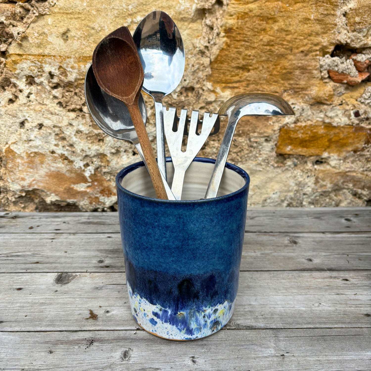 Blue ceramic container with kitchen utensils against a stone wall background