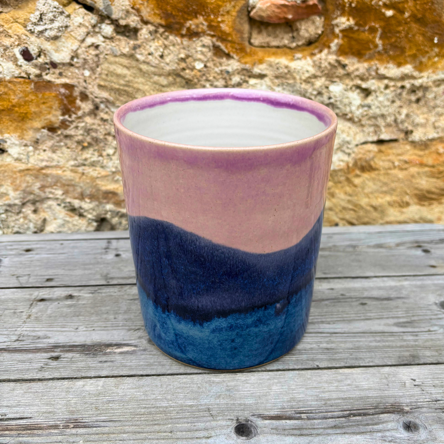 Ceramic utensil pot with purple and blue gradient on a wooden surface with stone wall background