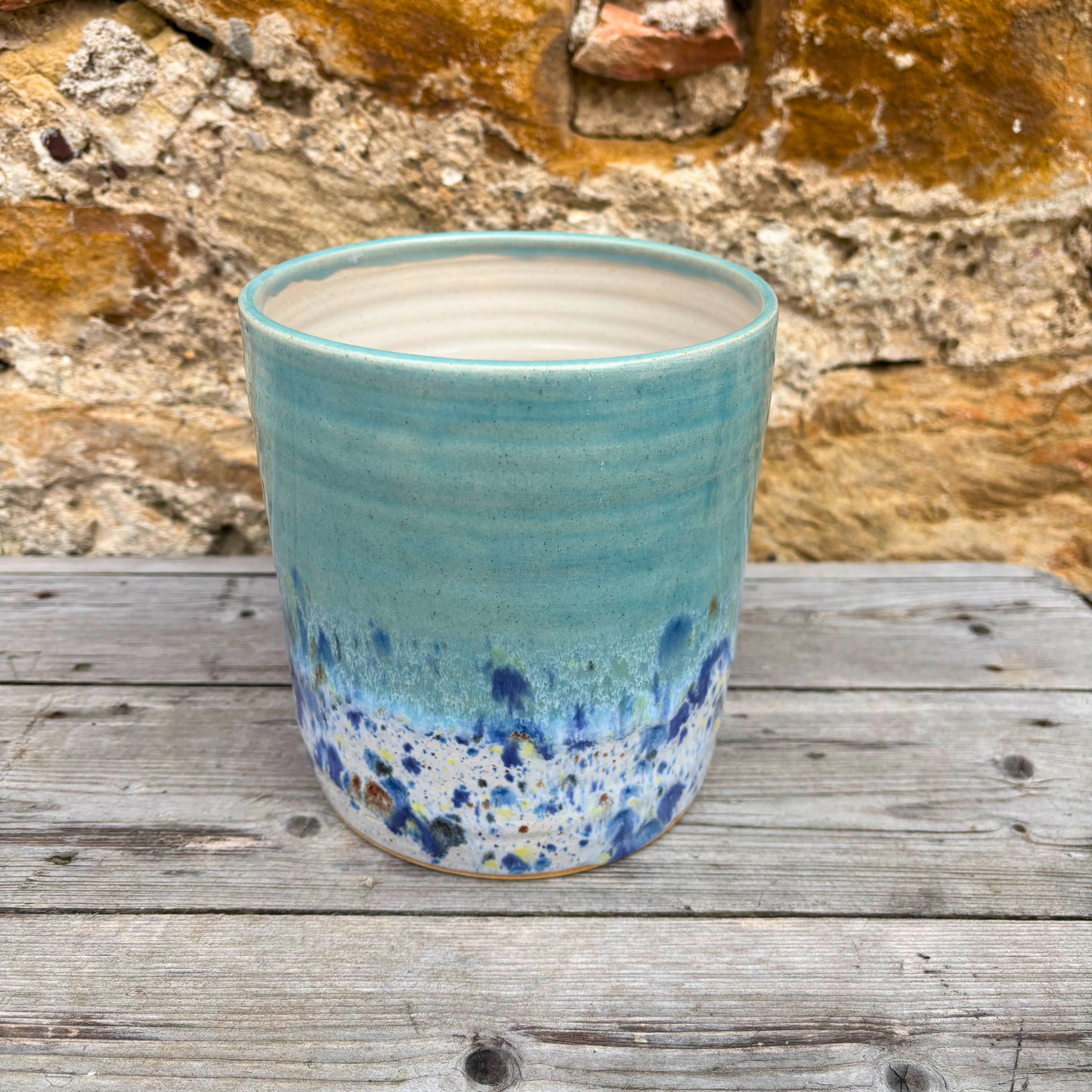 Blue ceramic pot with speckled design on a wooden surface with a stone wall background