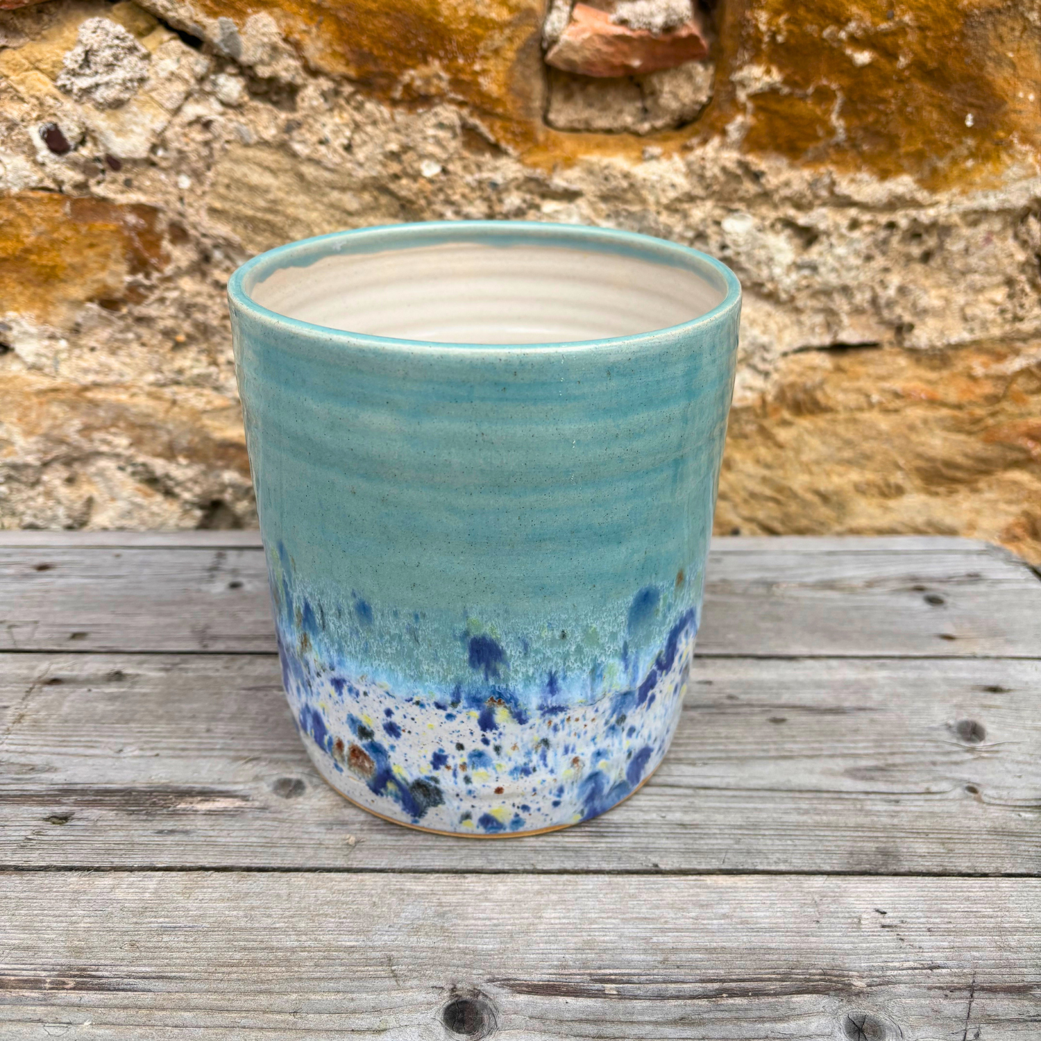 Blue ceramic pot with speckled design on a wooden surface with a stone wall background