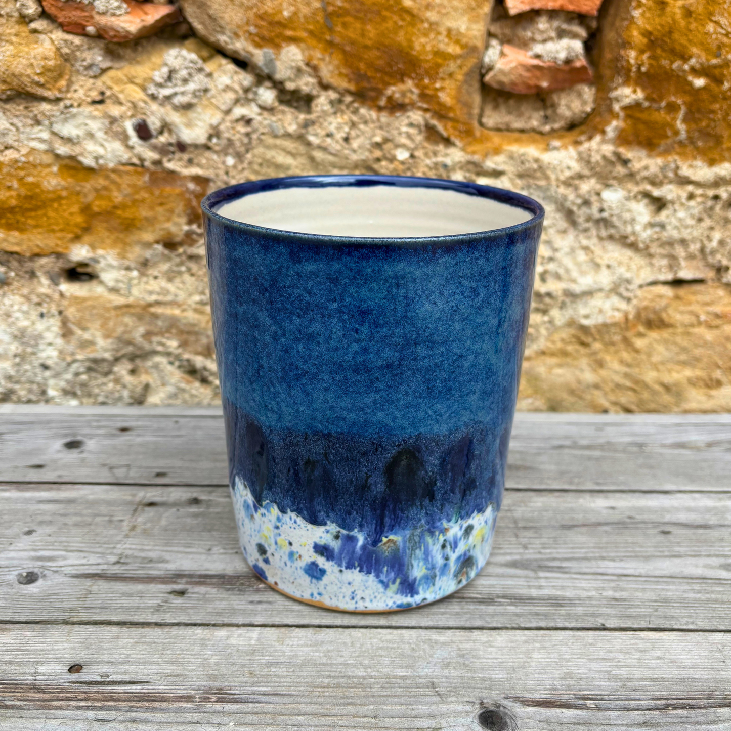 Blue ceramic utensil pot on a wooden surface with a rustic stone wall background