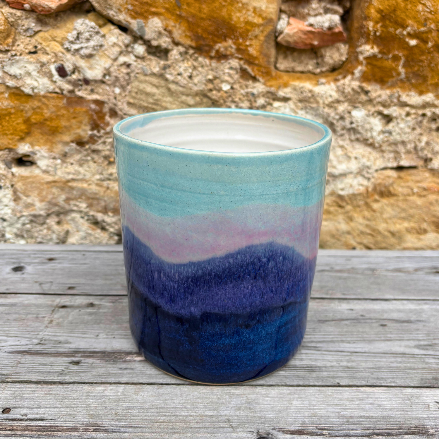 Colorful ceramic utensil pot with a gradient design on a wooden surface against a stone wall background.