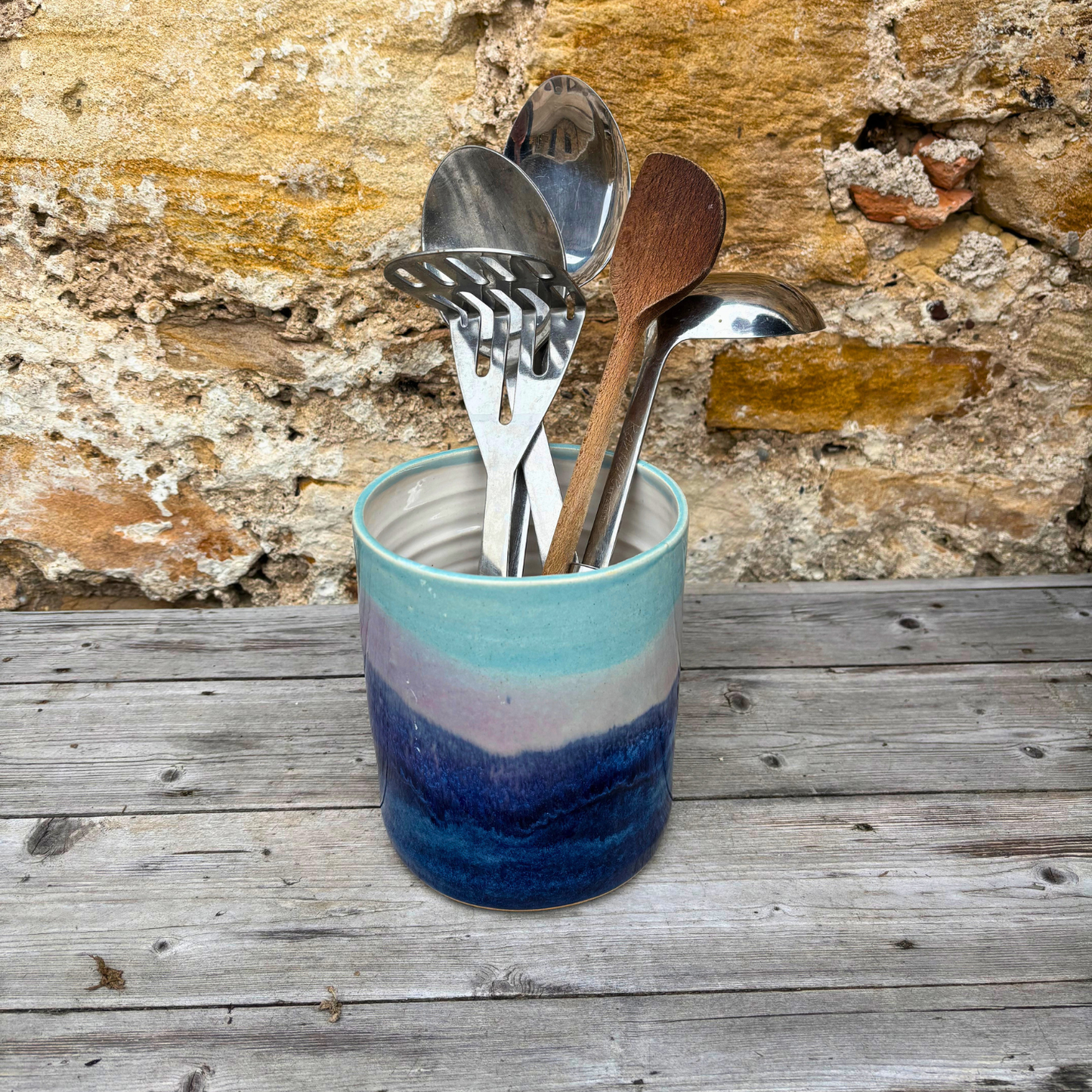 Colorful ceramic container with spoons against a stone wall background