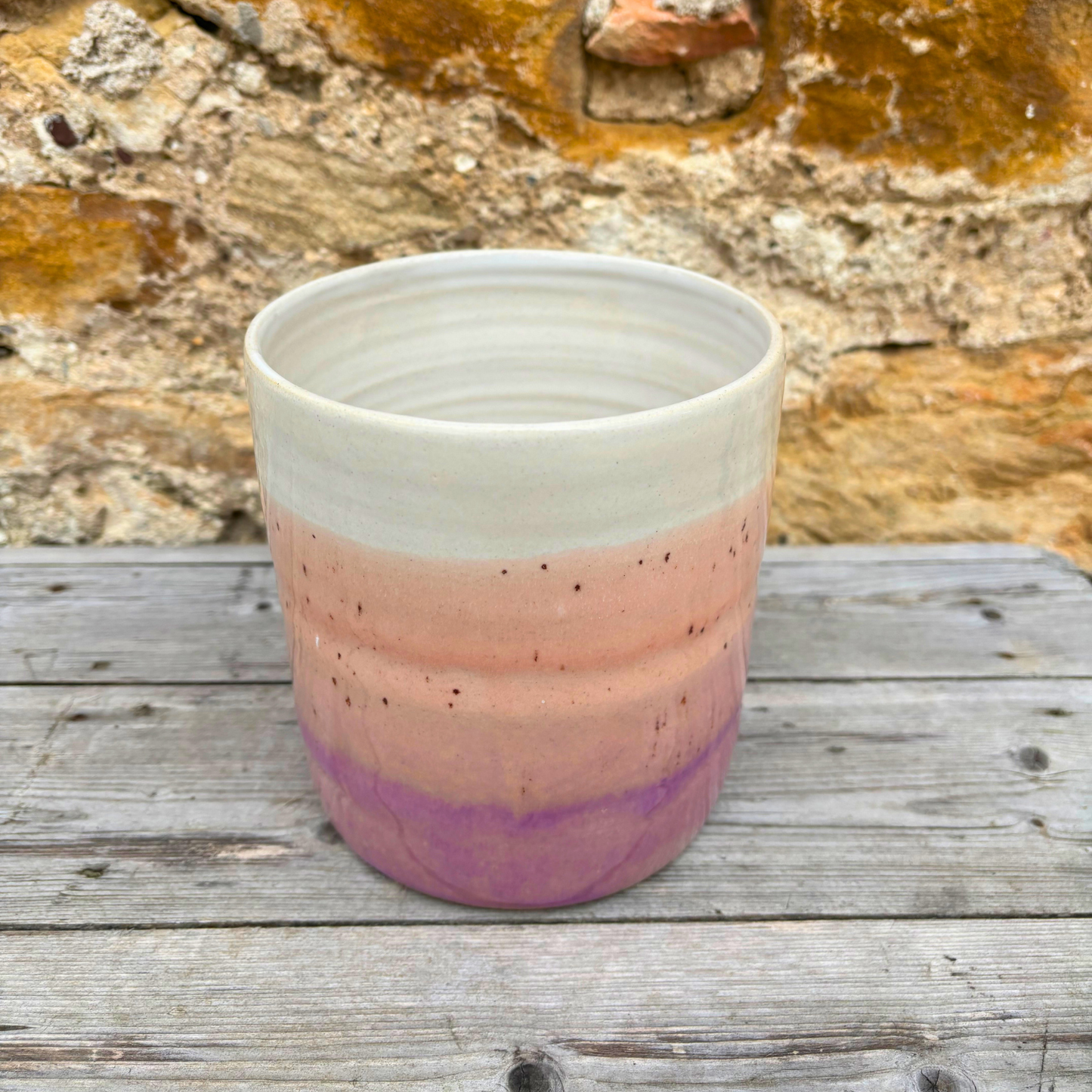 Hand holding a ceramic utensil pot  with a gradient design against a stone wall background