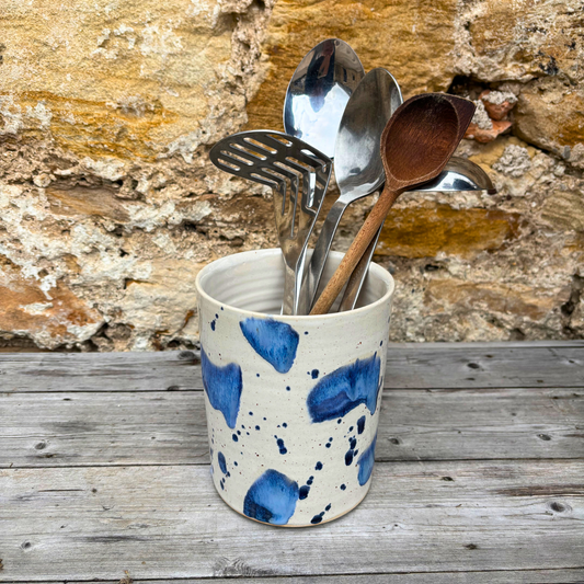 Ceramic cup with blue speckles holding kitchen utensils against a rustic stone wall.