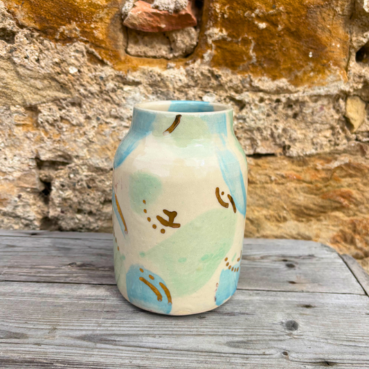 Ceramic vase with abstract design on a wooden surface against a stone wall background