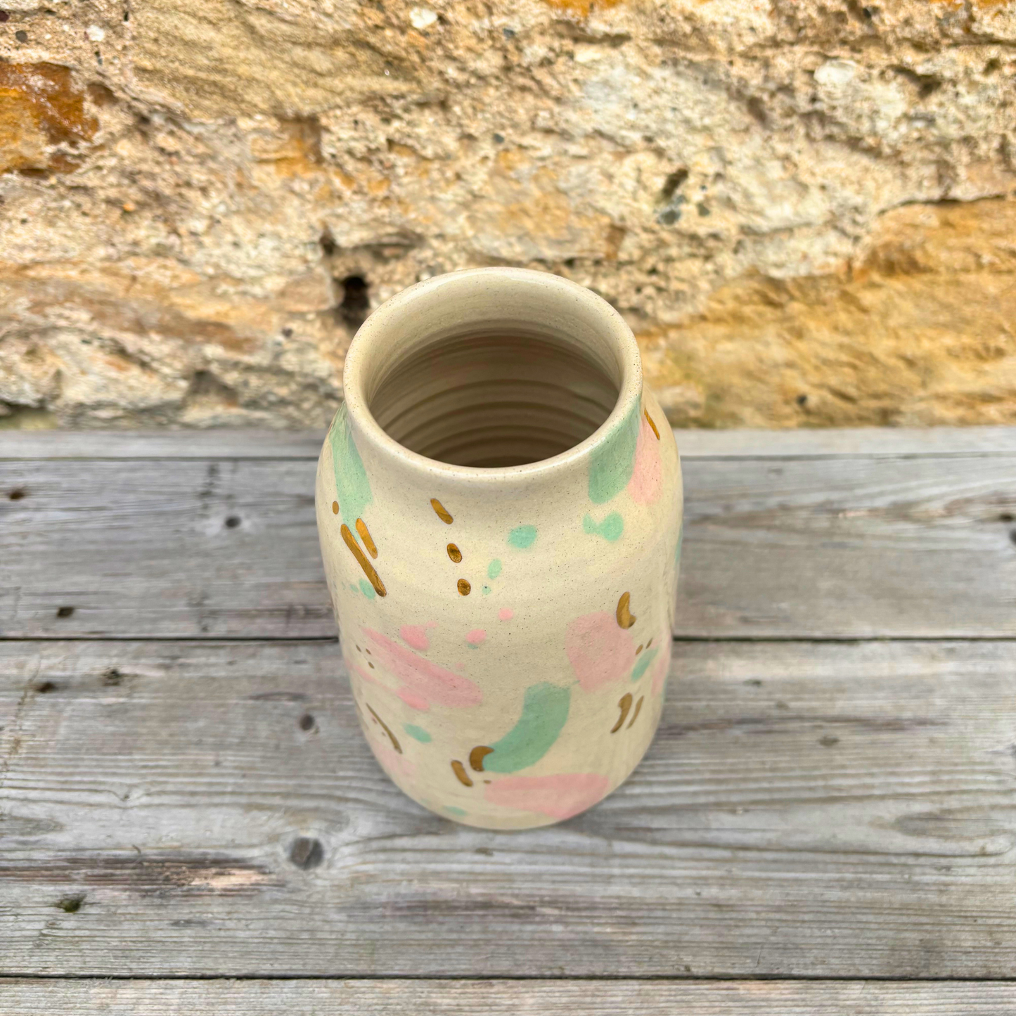 Handmade ceramic vase with abstract pastel designs on a wooden surface with a stone background