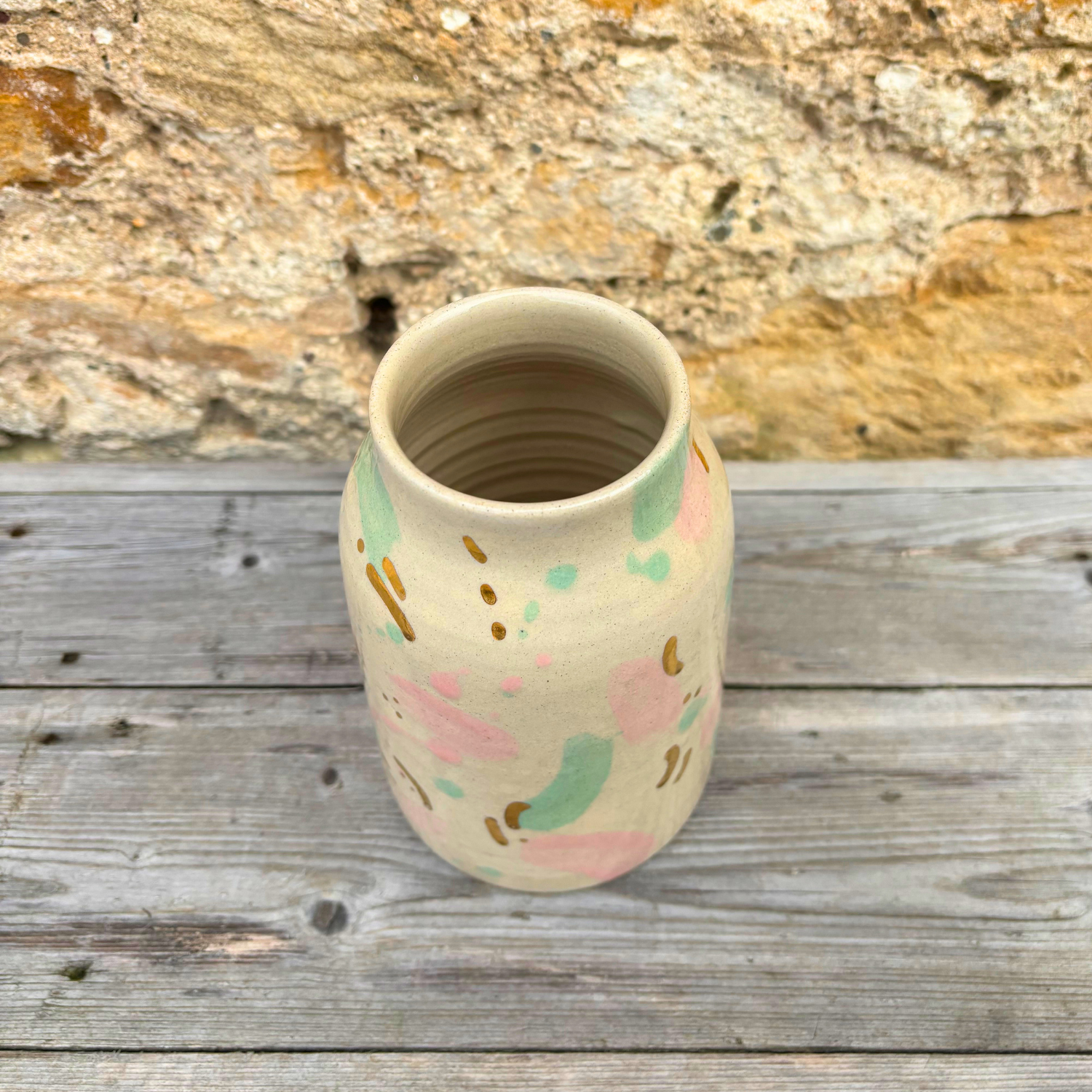 Handmade ceramic vase with abstract pastel designs on a wooden surface with a stone background