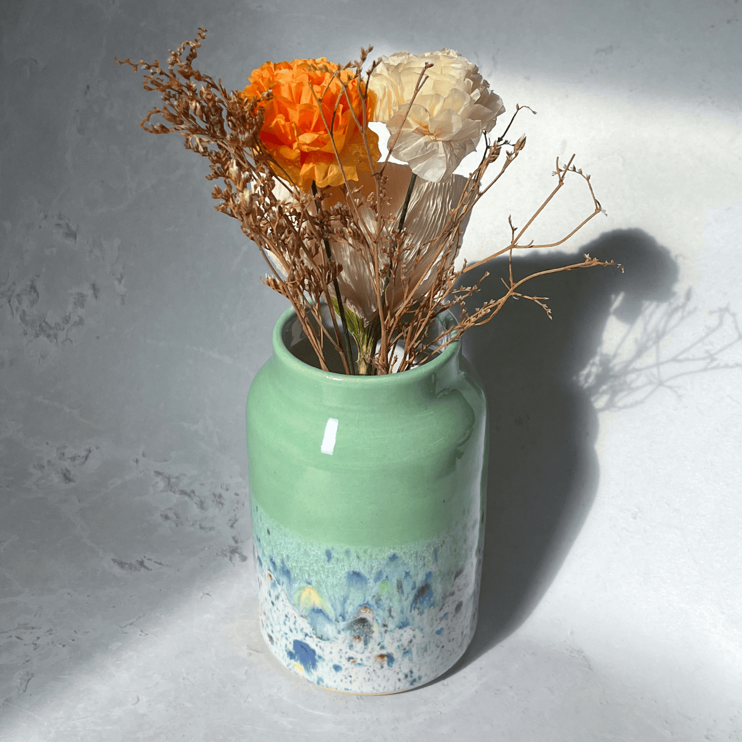 Ella Fletcher Designs Handmade Pottery Vase in Pale Green Shoreline Design - vase with solid green top and multi-coloured speckles at the bottom featuring flowers