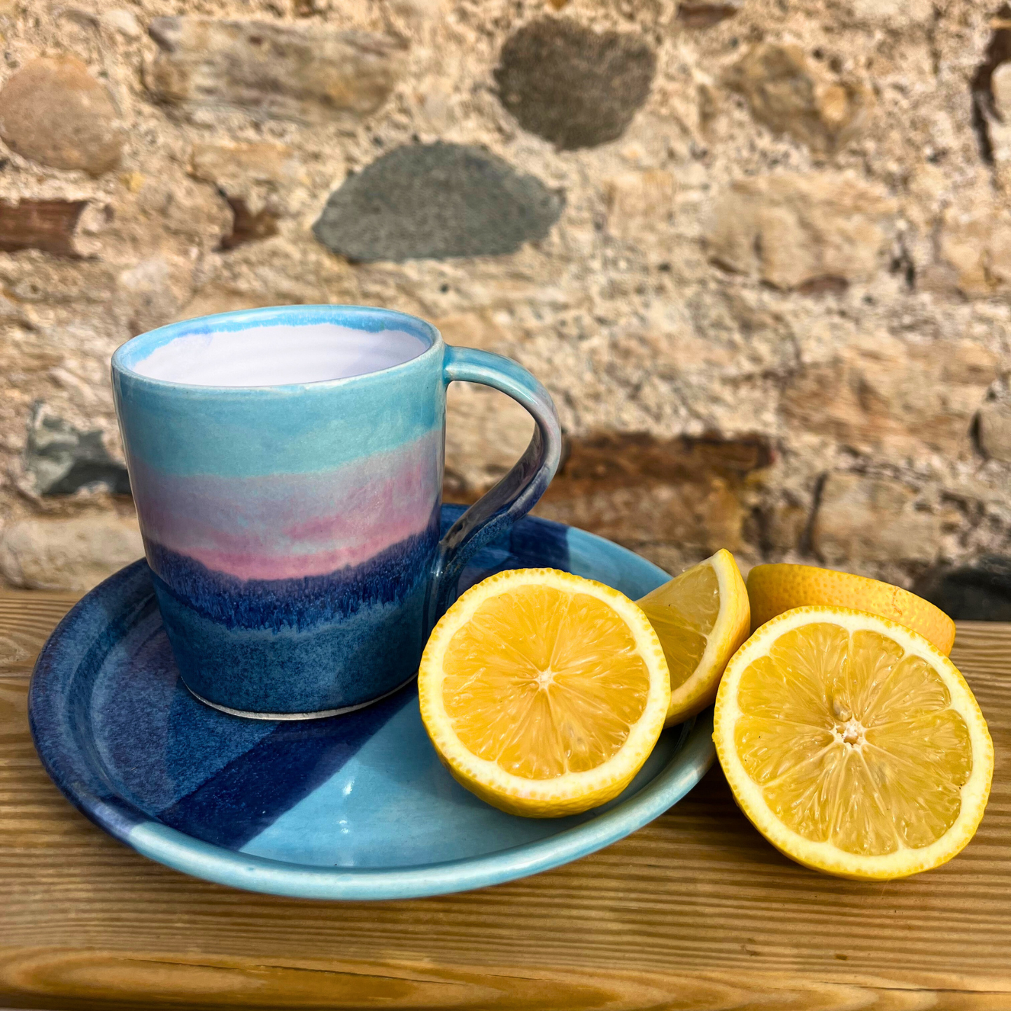 Blue ceramic mug and saucer with sliced lemons on a wooden surface against a stone wall background