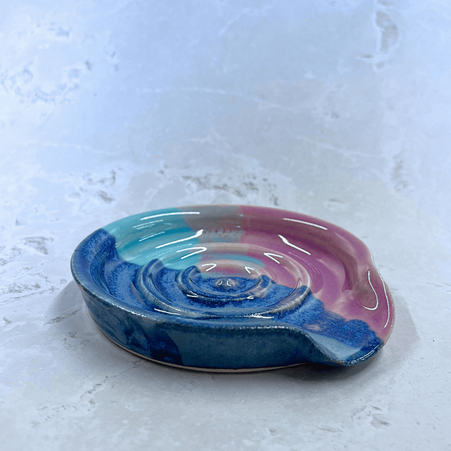 Ella Fletcher Designs Handmade Ceramic Spoon Rest in Scottish Sunrise Landscape design, side view of a circular spoon rest with raised edges in pink and blue layers inspired by the Scottish Sunrise