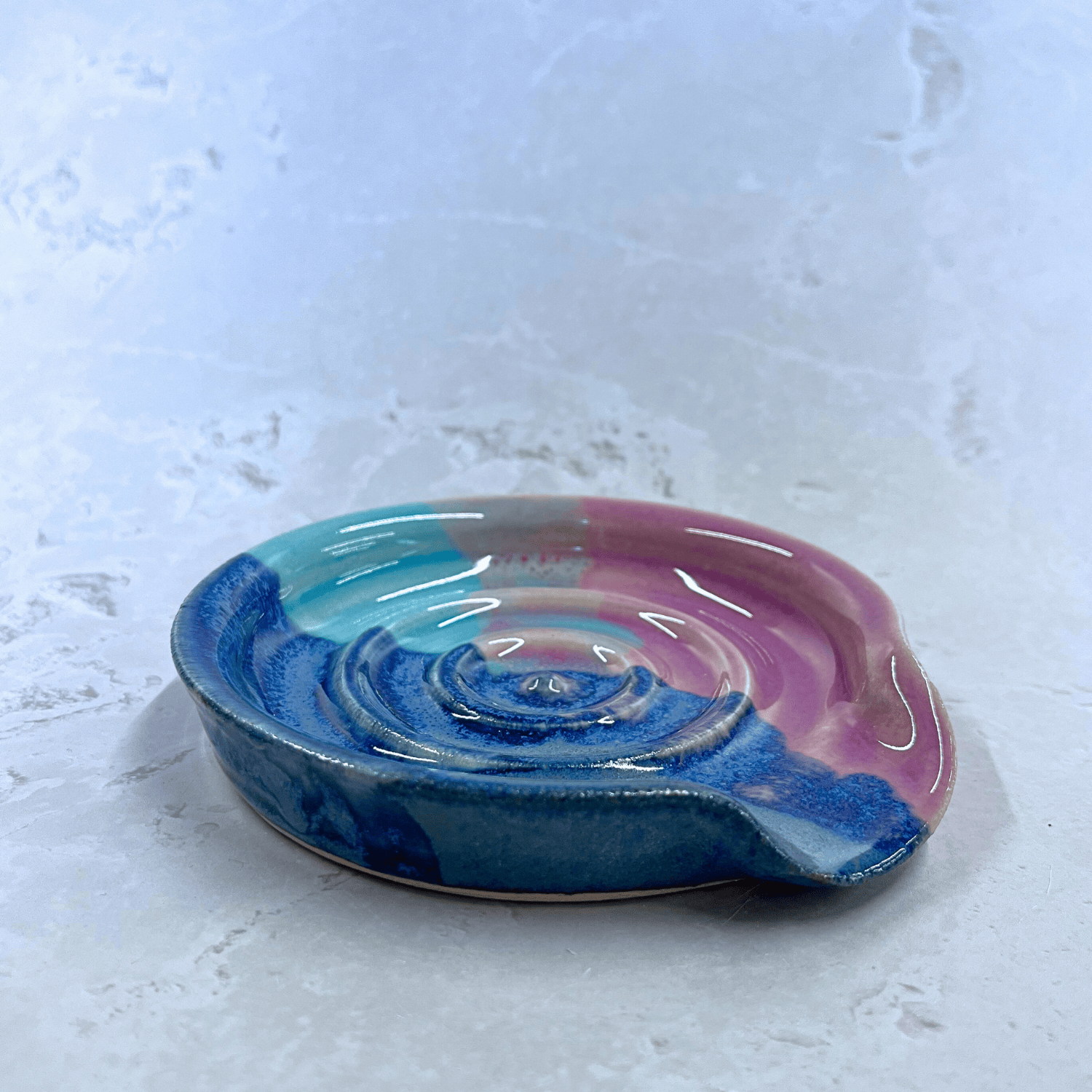Ella Fletcher Designs Handmade Ceramic Spoon Rest in Scottish Sunrise Landscape design, side view of a circular spoon rest with raised edges in pink and blue layers inspired by the Scottish Sunrise