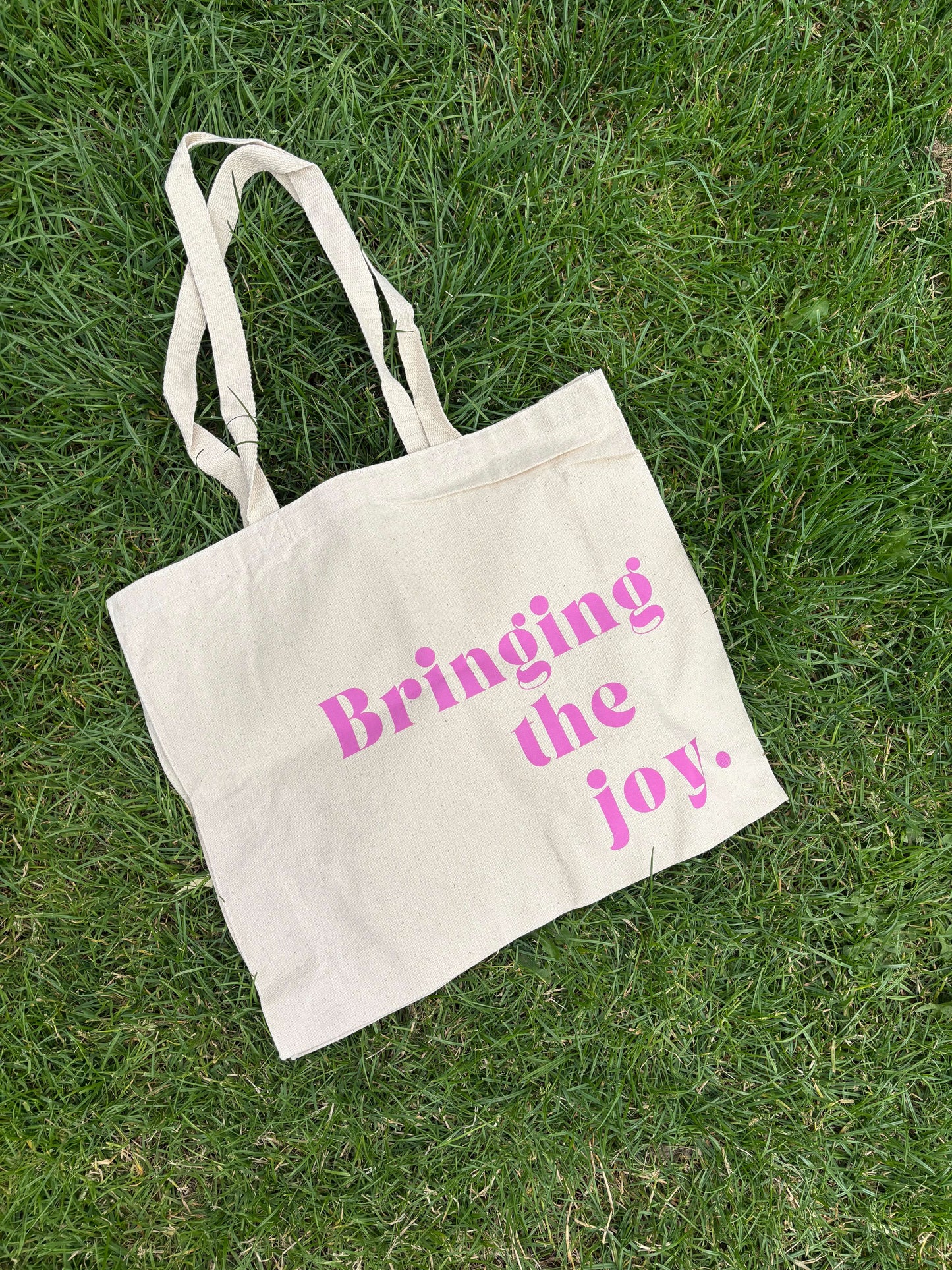 Ella Fletcher Designs Handmade Ceramics Tote Bag - Beige tote bag with 'Bringing the joy.' text on grass