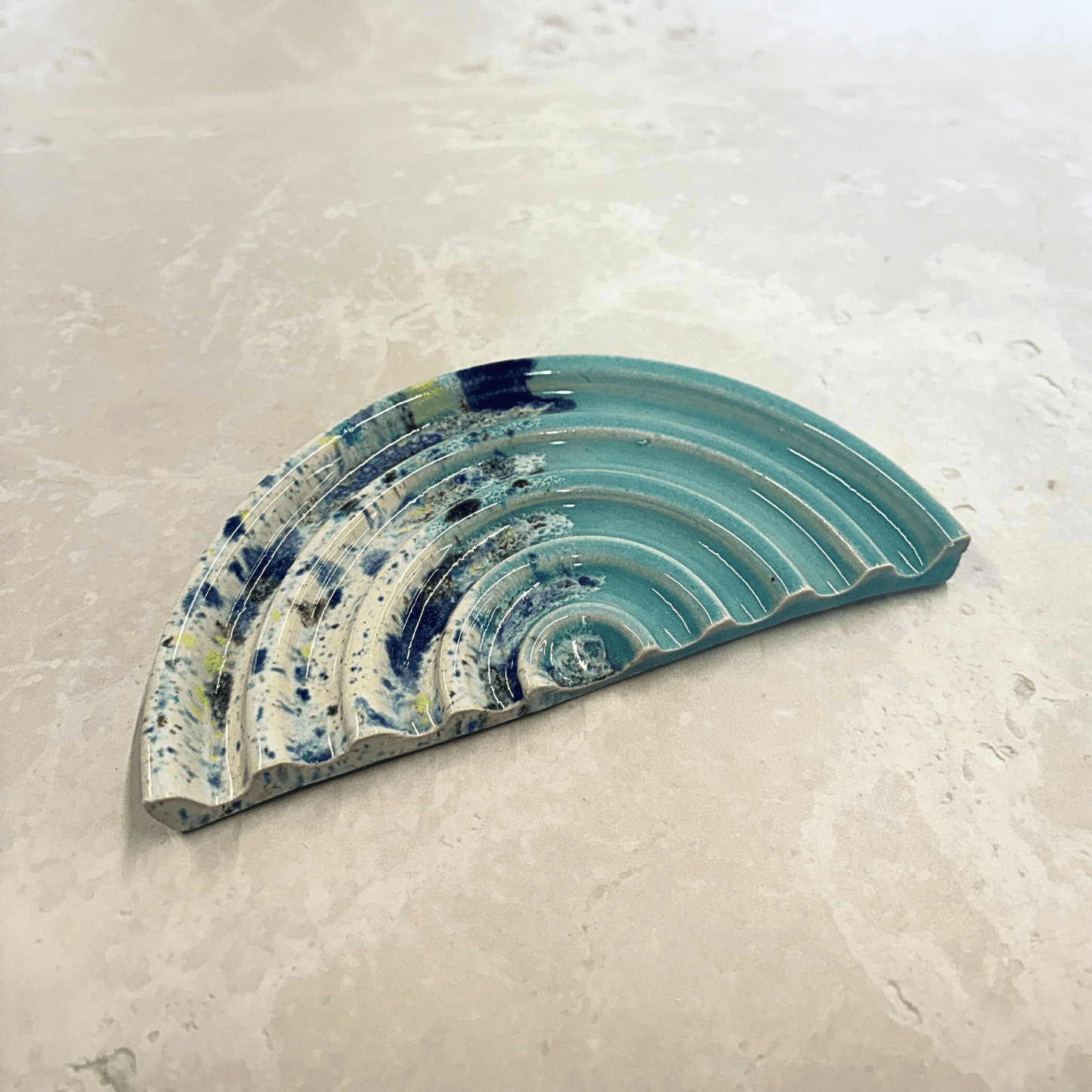 Ella Fletcher Designs Handmade Ceramics Soap Dish in Blue Shoreline design, semi-circle with grooved edges, half pale blue and half multi-coloured speckles