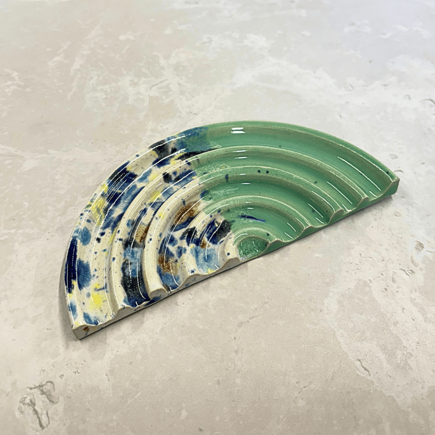 Ella Fletcher Designs Handmade Ceramic UK Soap Dish in Green Shoreline design, semi-circle with grooved edges, half pale green and half multi-coloured speckles