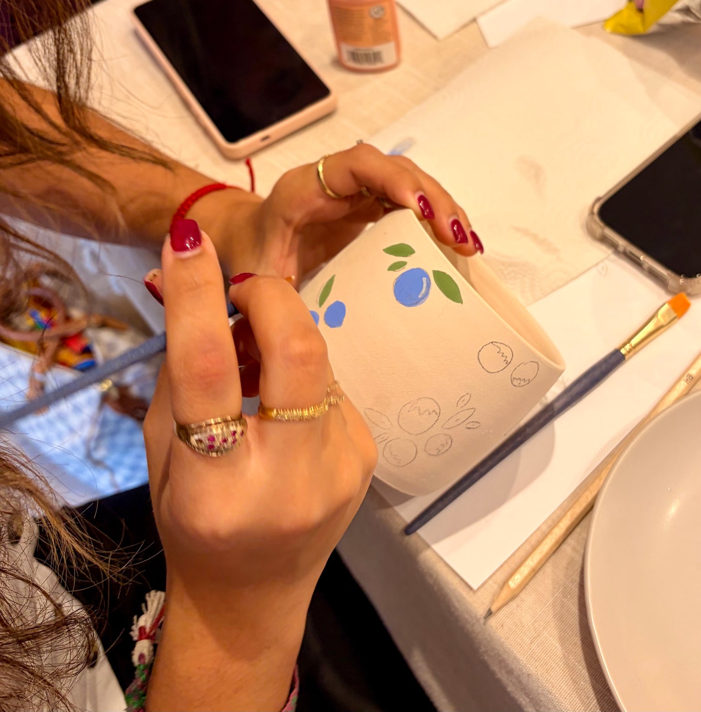Person holding a mug with blue and green decorations on a table with a phone and other items.