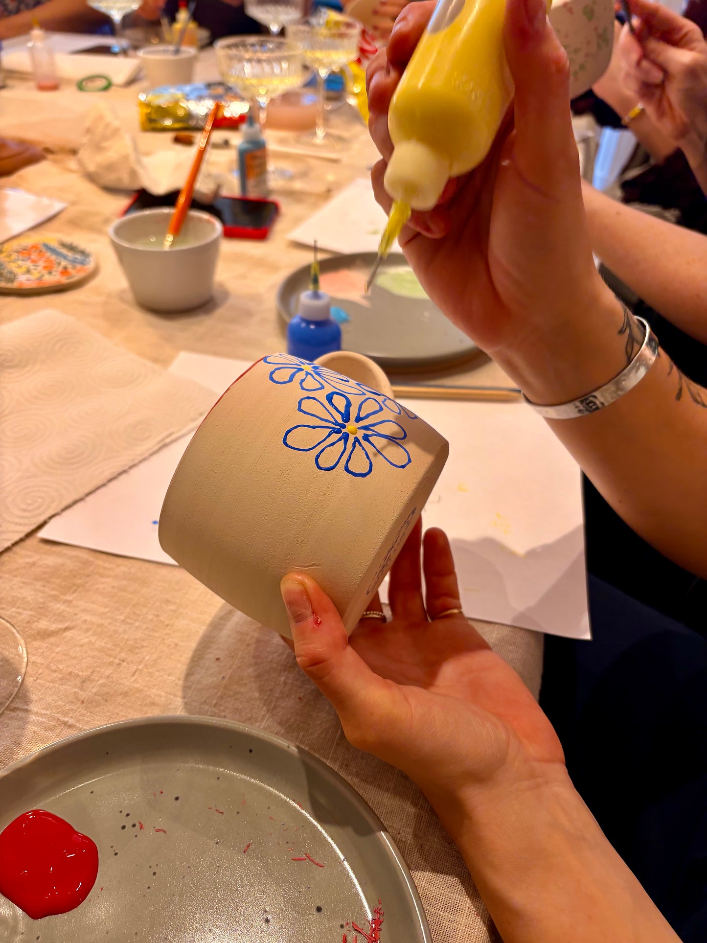 Person decorating a mug with blue icing on a table with art supplies.