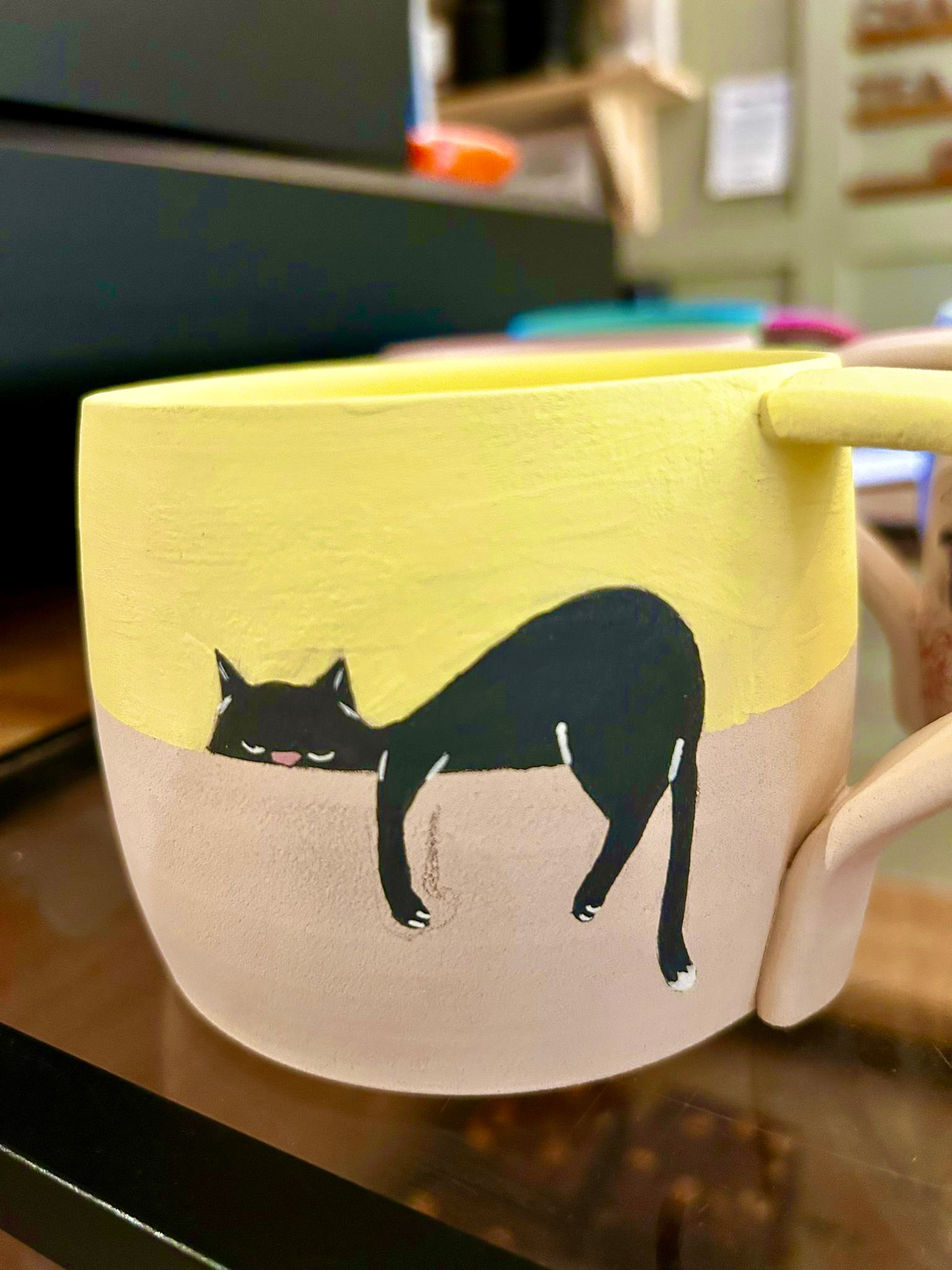 Yellow mug with a black cat design on a wooden surface