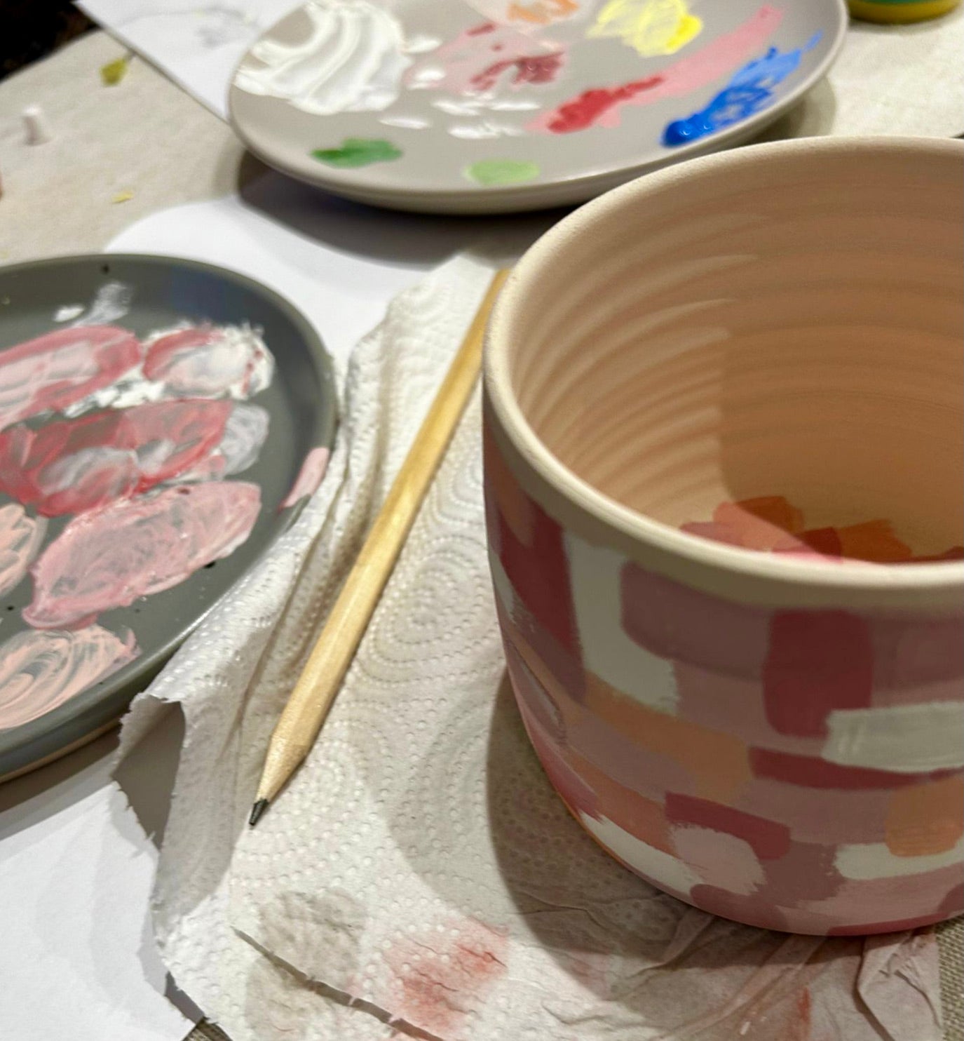 Painted ceramic cup with abstract design on a table with paint palettes and brush