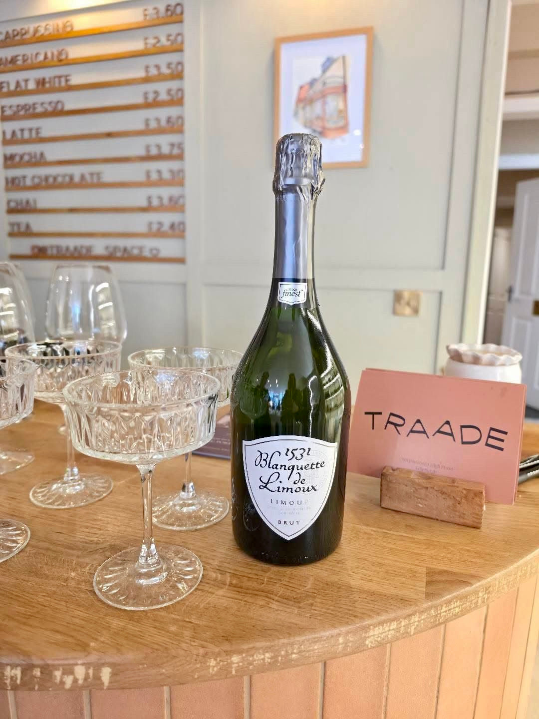 Bottle of champagne on a wooden table with glasses and a 'TRAADE' sign in the background.