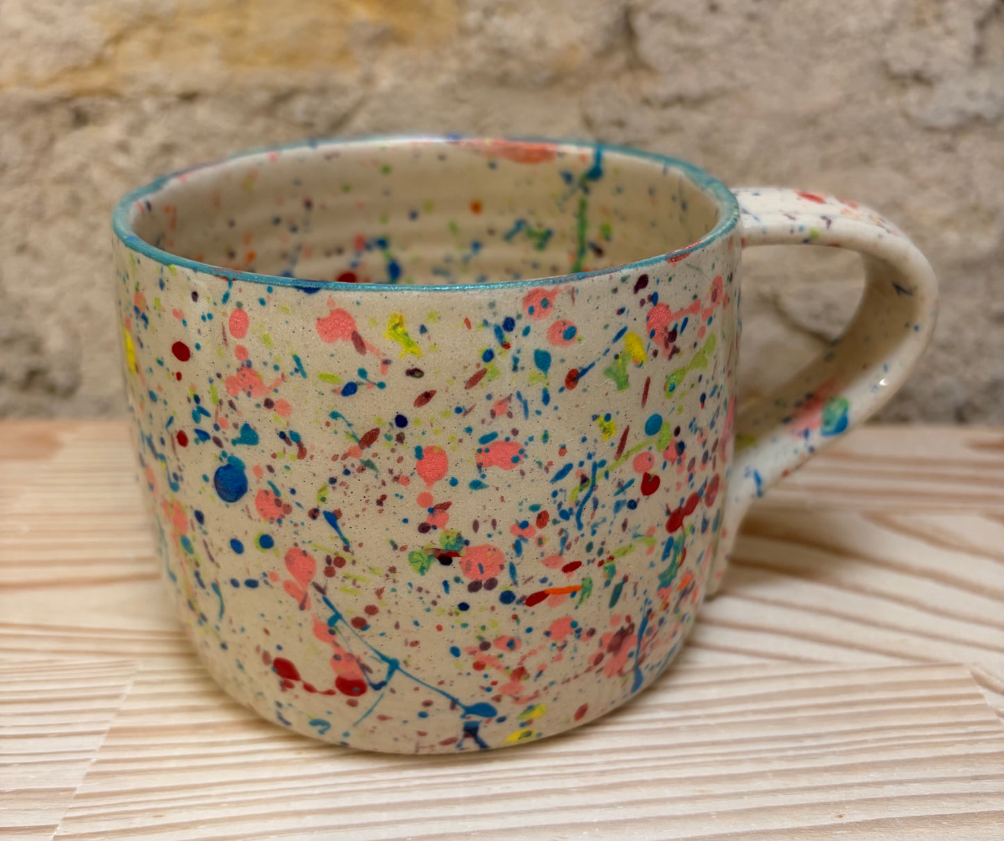 Speckled ceramic mug on a woven surface with a stone wall background