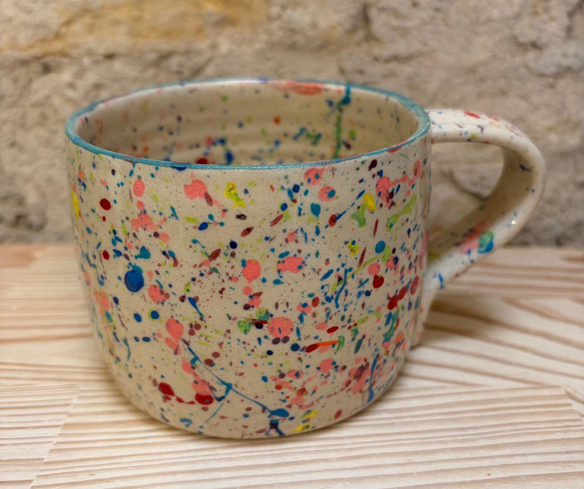 Speckled ceramic mug on a woven surface with a stone wall background